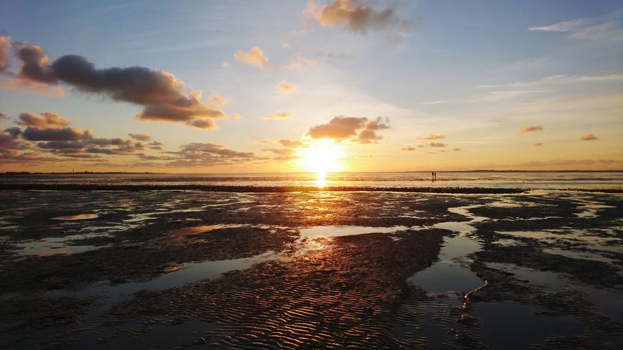 Lonely couple walking through the wattenmeer at the german north sea at sunset with low tide