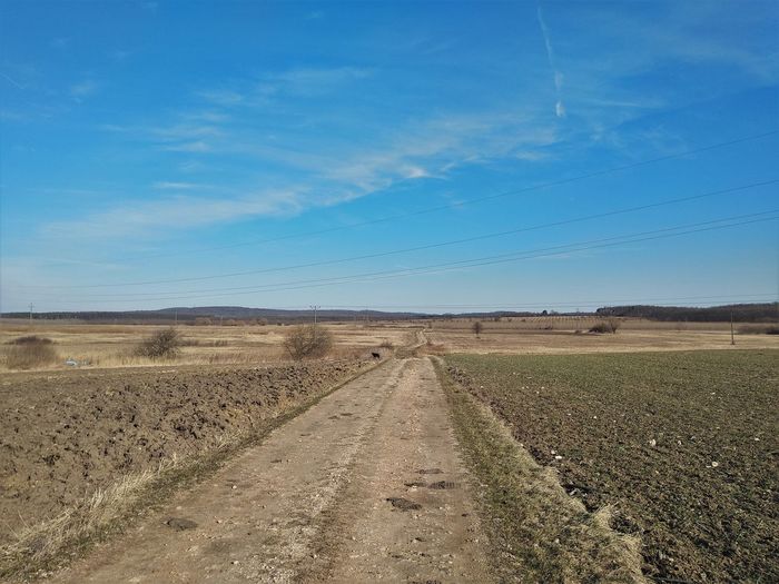 Dirt road on field against blue sky