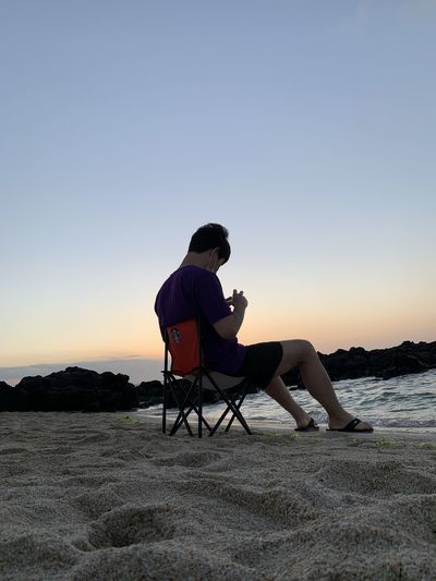 People sitting on seat against clear sky during sunset