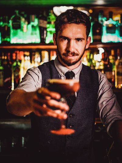Portrait of bartender holding drink while standing in bar