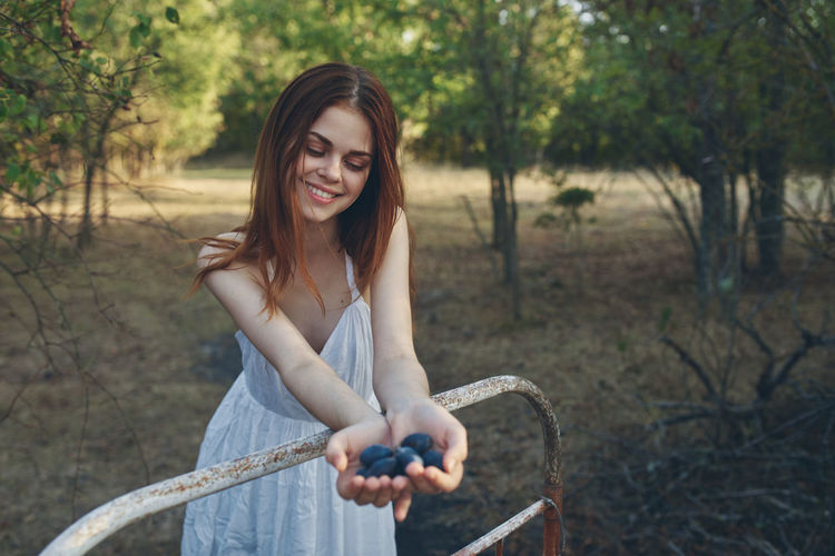 Young woman smiling while holding plants against trees