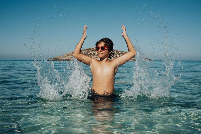 Boy playing with water on the beach in summer while wearing sunglasses