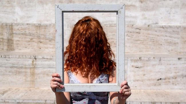 Woman with face covered in hair holding picture frame