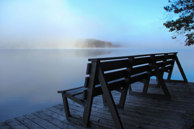 Empty bench on pier over lake during foggy weather