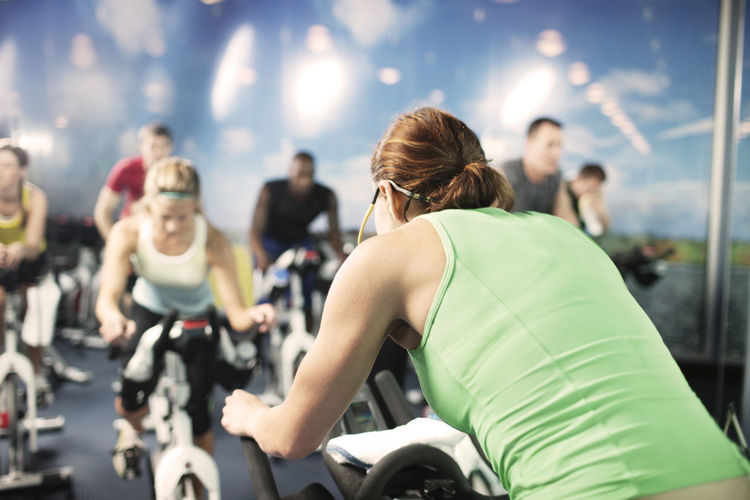 Fitness instructor with clients riding exercise bikes at gym