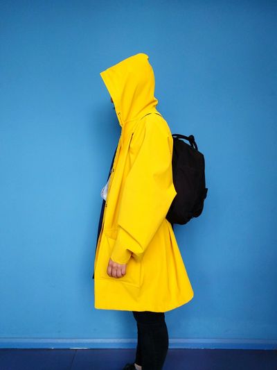 Side view of woman wearing yellow raincoat against blue wall