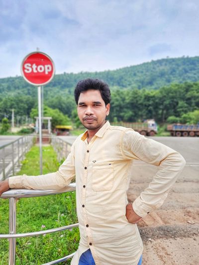 An adult person standing in front of a stop sign board of the traffic chowk. 