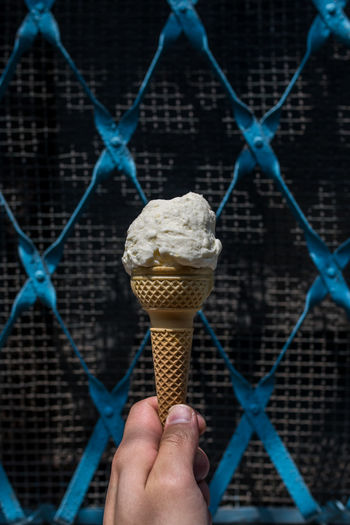 Cropped image of hand holding ice cream cone against fence