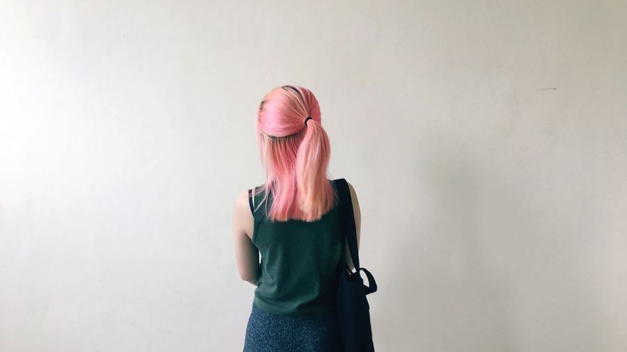 Rear view of woman with dyed hair standing against wall