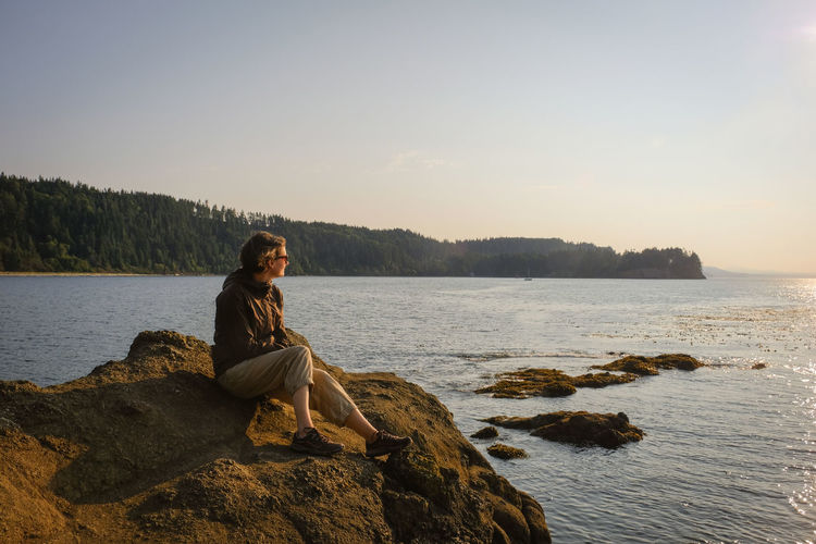 Full length of woman sitting on rock in sea against sky