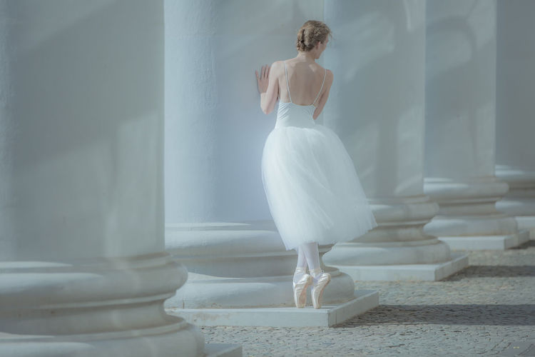 Rear view of woman ballet dancer standing against building 
