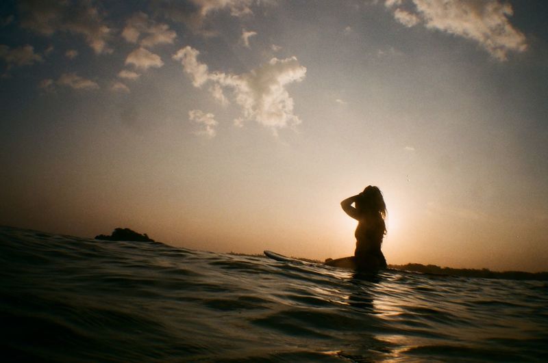 Full length of woman standing in sea against sky during sunset