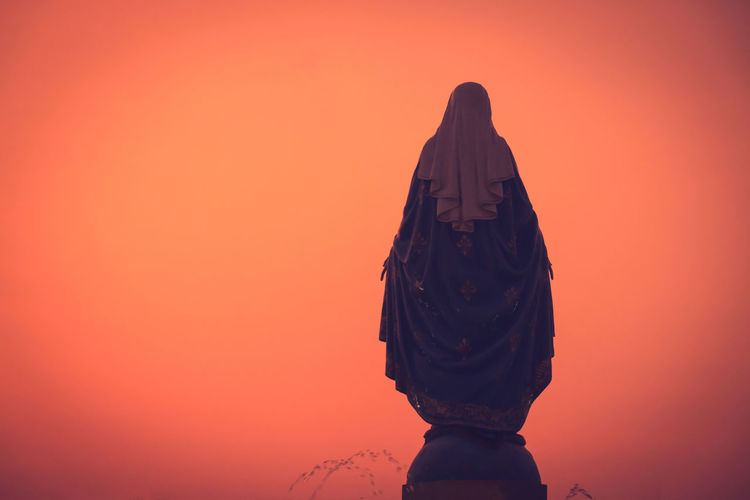 Rear view of woman statue against orange sky