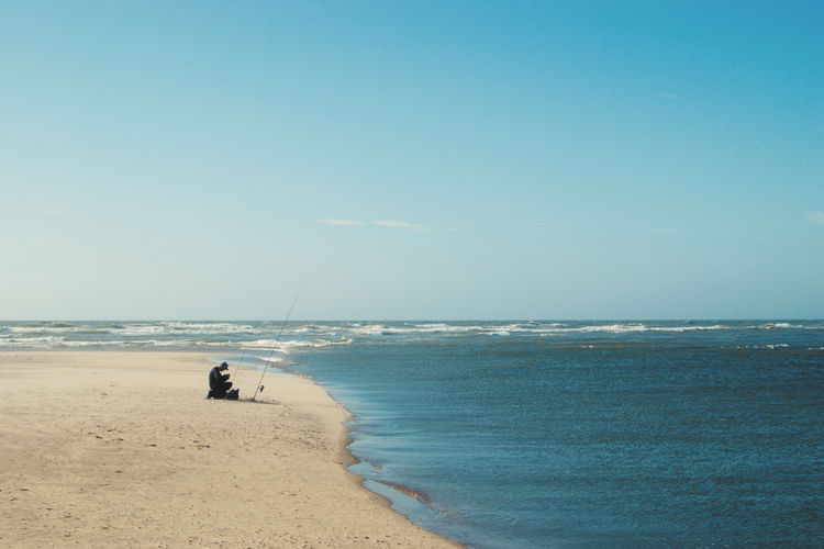 Side view of man sitting at beach against blue sky