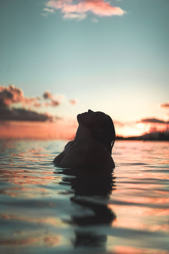 Silhouette swimming in sea against sky during sunset