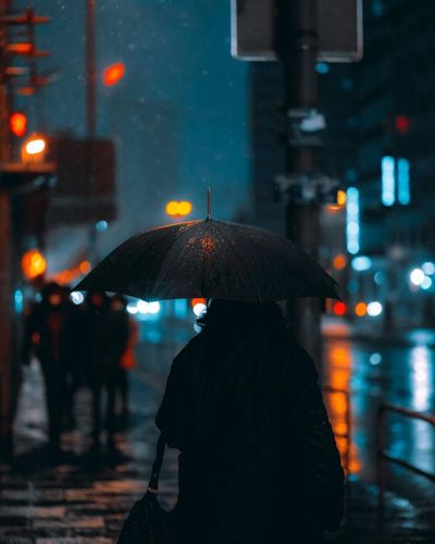 Rear view of woman walking on wet street during rainy season