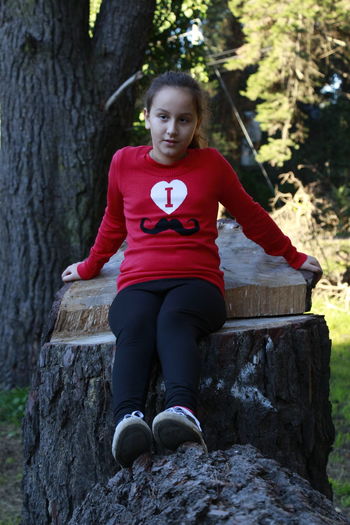 Portrait of teenage girl sitting on tree trunk