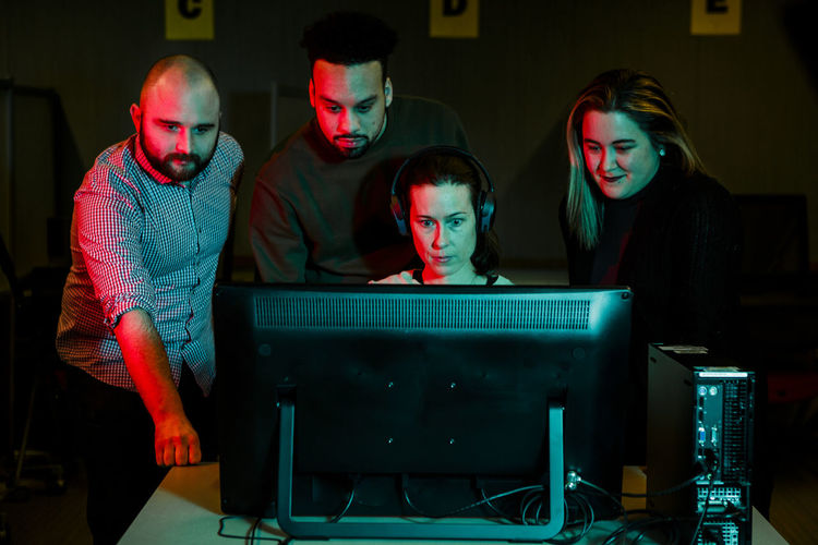 A woman gathers a team of students around computer in dark room