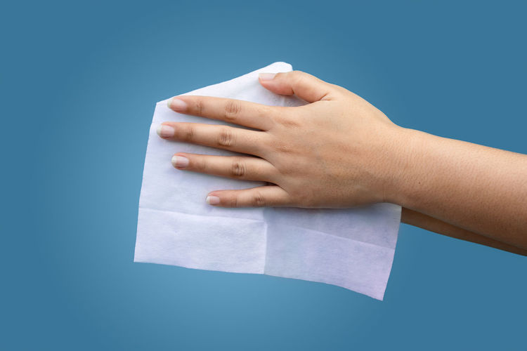 Close-up of hand holding paper against blue background