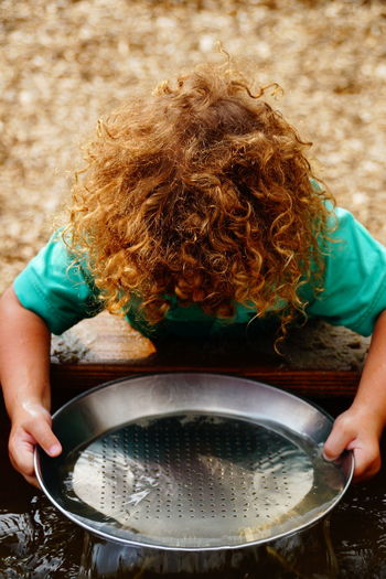 High angle view of boy with blond curly hair washing plate in trough