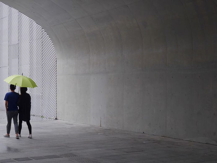 Rear view full length of people with umbrella below bridge during rainy season