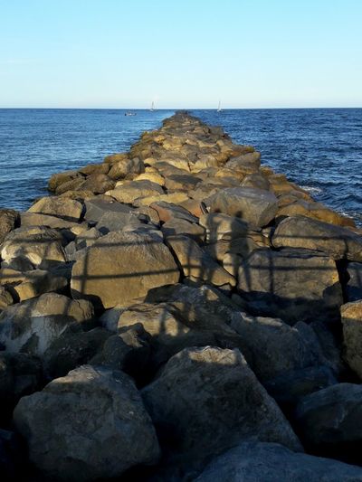 Rocks on shore by sea against clear sky