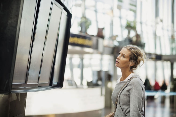 Side view of businesswoman reading arrival departure board at airport