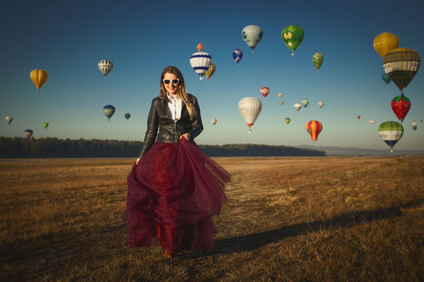 Portrait of woman walking against hot air balloons flying in clear blue sky