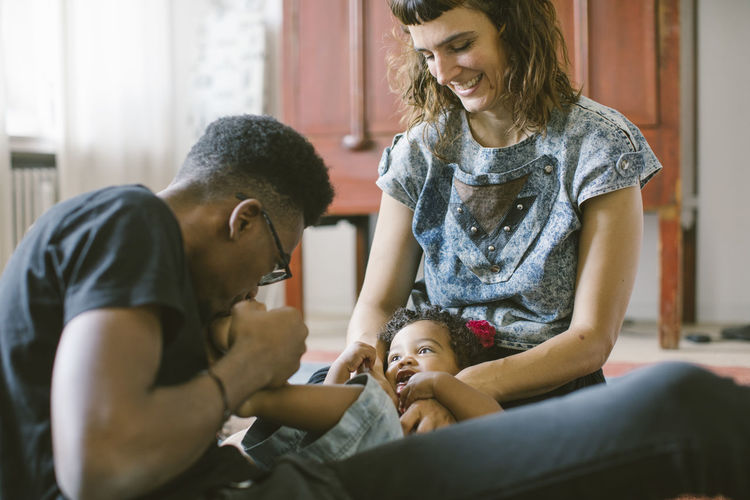 Father kissing foot of daughter lying on mother's lap at home