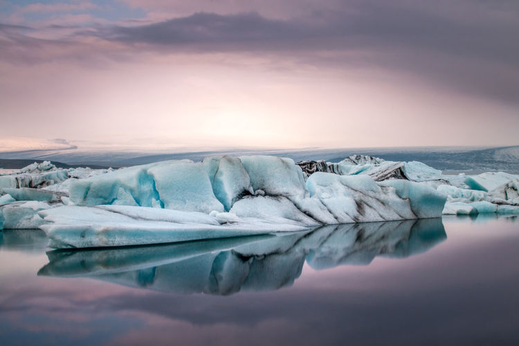 Icebergs in lagoon against cloudy sky during sunset