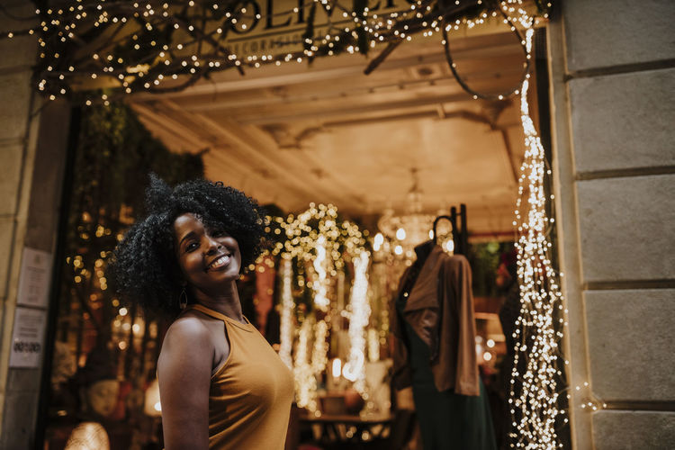 Smiling woman standing by illuminated store at night