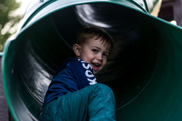 Low angle portrait of cheerful boy sitting in slide