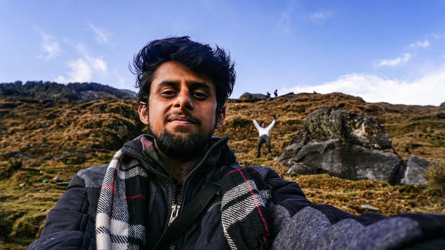 Portrait of man with friend standing in background on mountain against sky