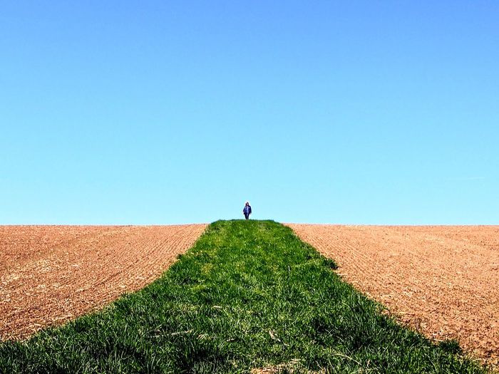 Woman walking on agricultural field against clear blue sky