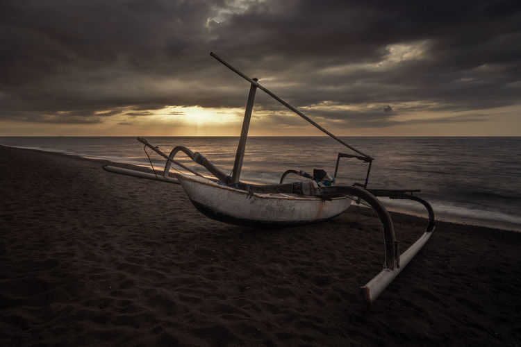 Fishing boat on beach against sky during sunset