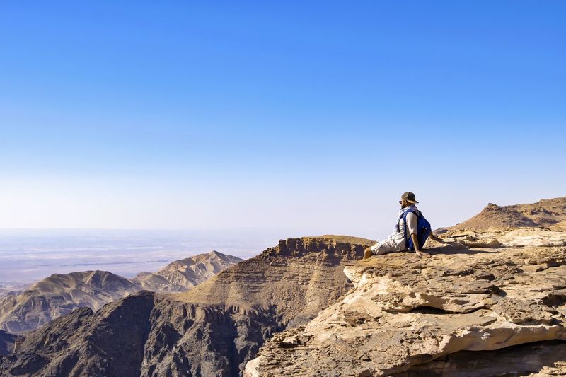 Man sitting on cliff against clear sky