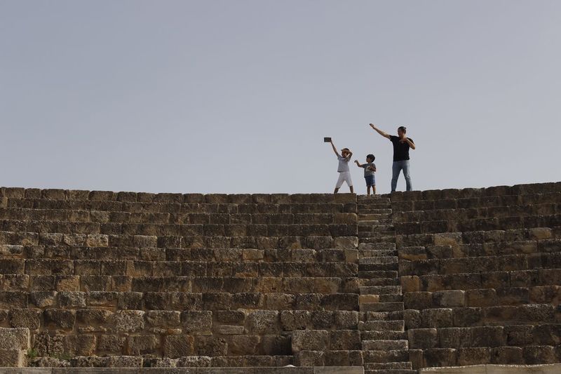 Low angle view of father with sons standing on retaining wall against clear sky