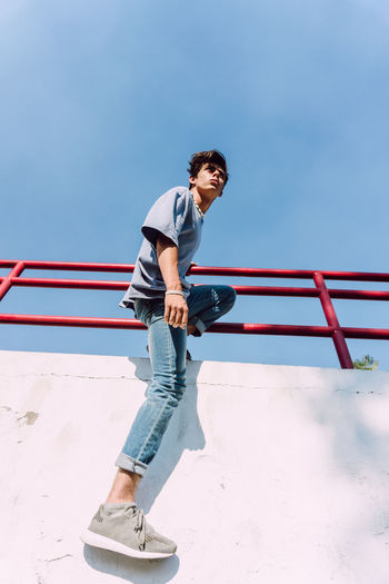 Full length of young man standing on railing against sky