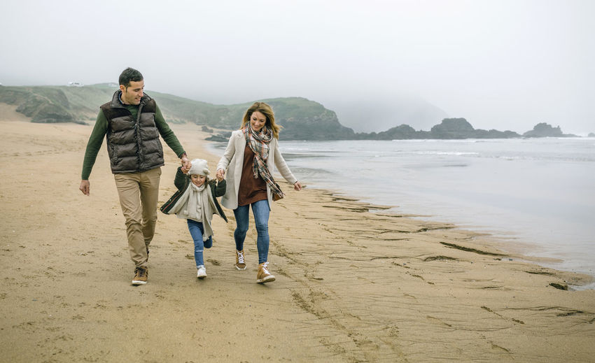 Happy family with daughter walking on the beach in winter