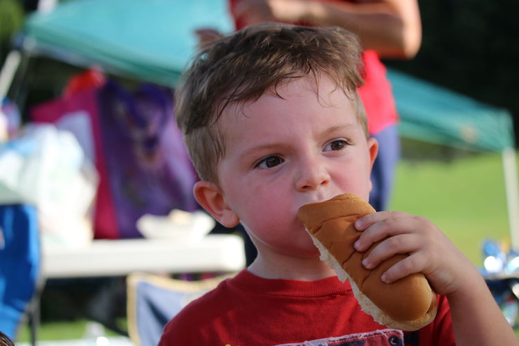Close-up of boy eating hot dog while standing at park