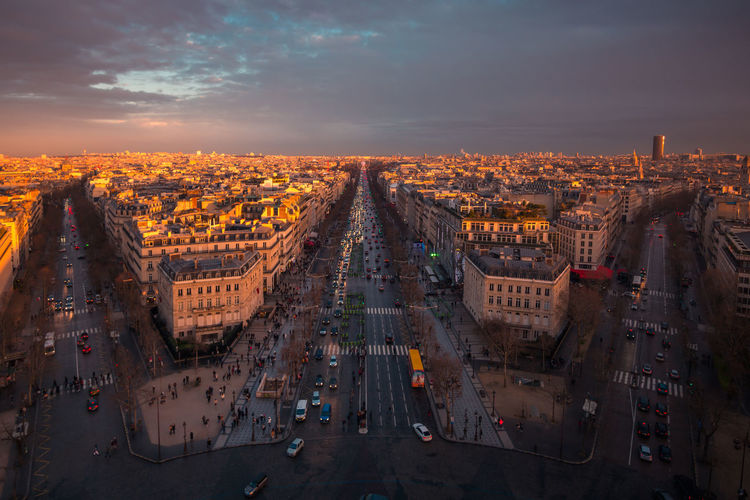 Drone view of urban house facades and roadways with transport under shiny cloudy sky at sundown in paris france
