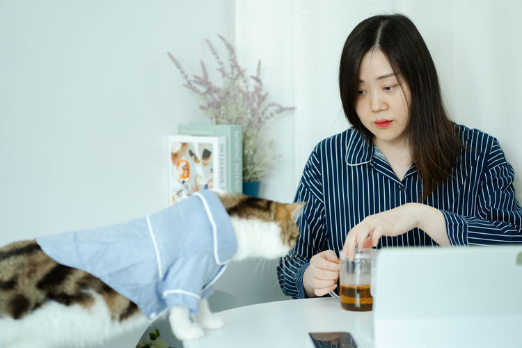 Woman in pajamas cloth drink tea and play with her cat