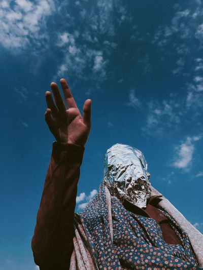 Low angle view of woman with covered face standing against sky