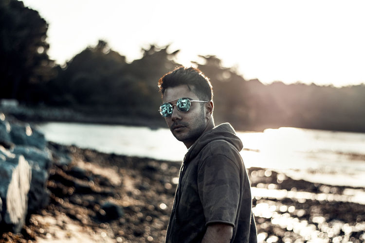 Side view of young man wearing sunglasses standing against sky