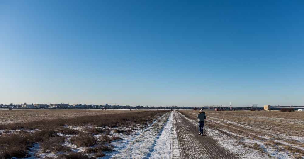 Man walking on snowy field against clear blue sky