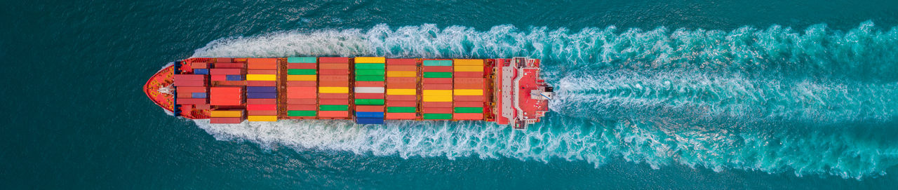 Aerial top view of cargo ship with contrail in the ocean sea ship carrying container and running 