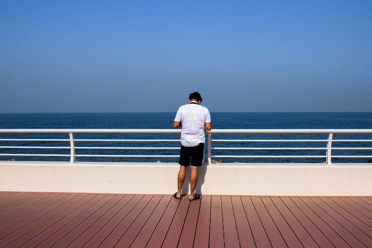 Rear view of man standing on jetty against sea