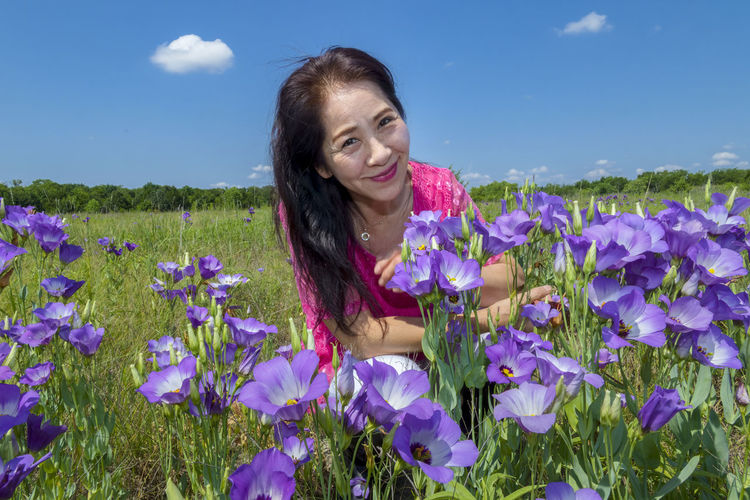 Portrait of smiling young woman with purple flowers on field