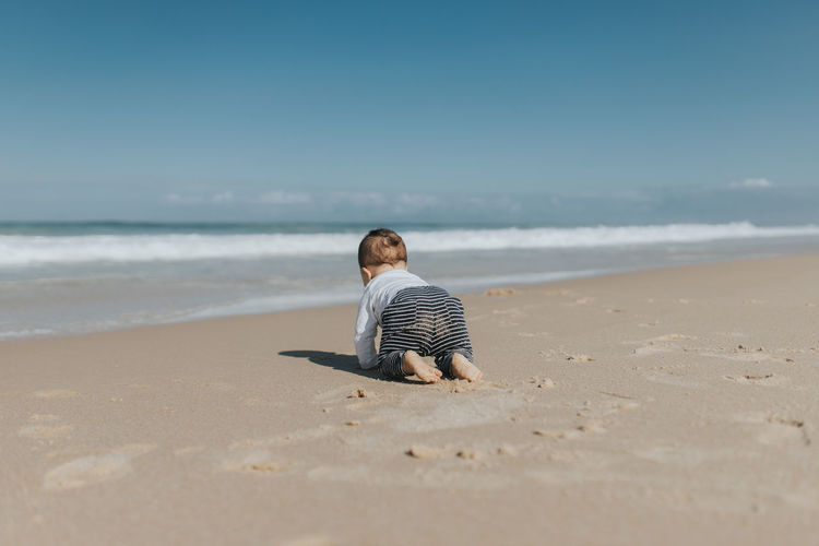 Rear view of cute boy crawling on beach