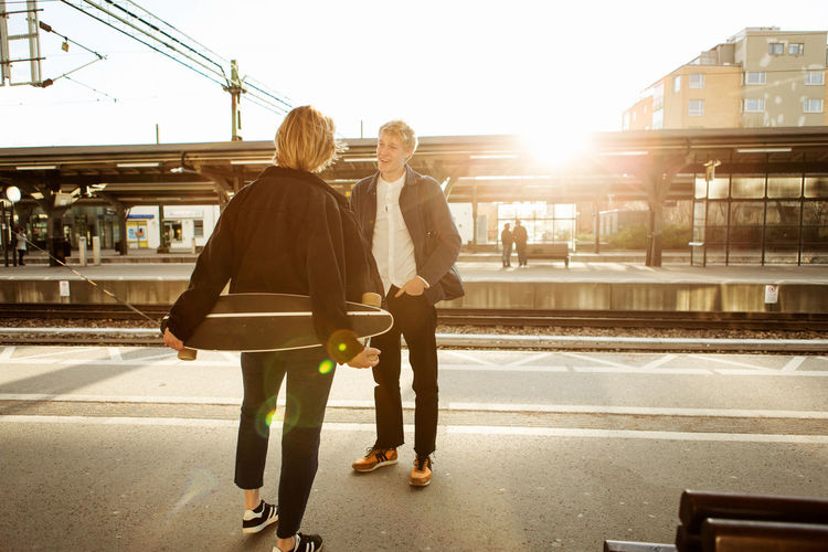 Happy young man talking with teenage girl while standing on railroad station platform